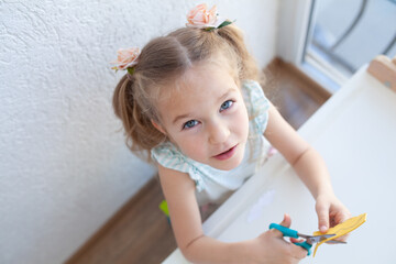 The girl cuts and sculpts from plasticine, is engaged in creativity at a white table against a white wall, early childhood development, kindergarten