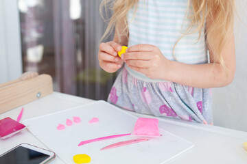 The girl cuts and sculpts from plasticine, is engaged in creativity at a white table against a...