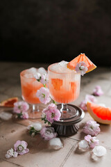 Grapefruit cocktail with ice and flowers in beautiful transparent glasses on a beige table. Simple fruit juice with food styling.
