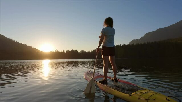 Adventurous Woman Paddling On A Paddle Board In A Peaceful Lake. Sunny Sunset. Hicks Lake, Sasquatch Provincial Park Near Harrison Hot Springs, British Columbia, Canada. Slow Motion