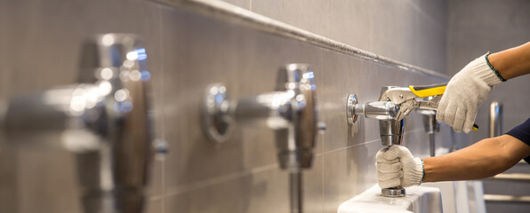 A handyman or plumber is using a wrench to fix or repair leaking water pipes, faucets or valves in sinks and toilet bowls.