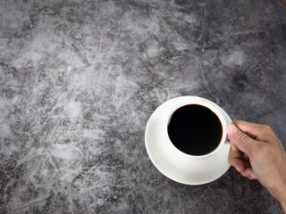 Close up hand holding black coffee cup dark background top view