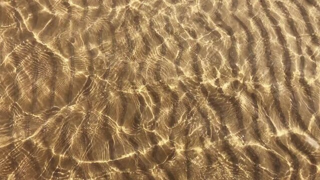 Transparent water ripples and gold sand with waves, sunlight glare. Sea floor pattern background.