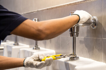 A handyman or plumber is using a wrench to fix or repair leaking water pipes, faucets or valves in...