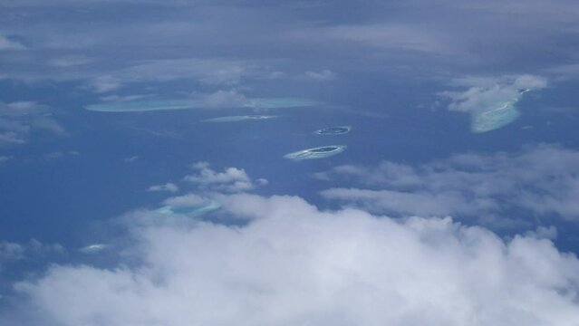 Clouds fly over the blue ocean and tropical islans reflecting on the surface of the water, aerial shot in the Indian Ocean