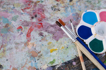 Dirty palette with different paints and paintbrush on dirty table. Lifestyle and hobby...