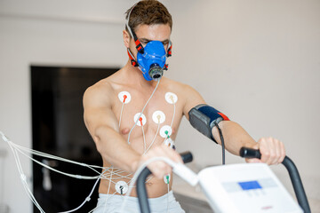 Man athlete with breath mask and electrodes training on bike simulator, examining his...
