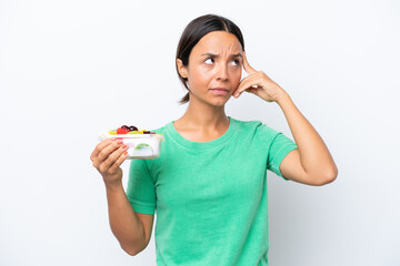 Young hispanic woman holding a bowl of fruit isolated on white background having doubts and thinking