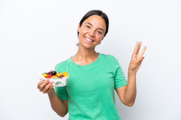 Young hispanic woman holding a bowl of fruit isolated on white background happy and counting three with fingers