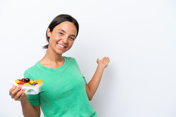 Young hispanic woman holding a bowl of fruit isolated on white background extending hands to the side for inviting to come