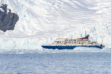 Expedition ship in front of Antarctic iceberg landscape in Cierva Cove - a deep inlet on the west side of the Antarctic Peninsula, surrounded by rugged mountains and dramatic glacier fronts.