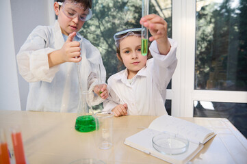 Obraz premium Beautiful Caucasian baby girl analyzing test tube with green chemicals and handsome smart child boy using a measuring pipette pipetting few reagents into a flat bottomed flask, during Chemistry lesson