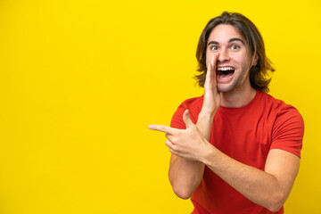 Caucasian handsome man isolated on yellow background pointing to the side to present a product and whispering something