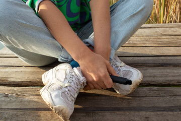 Woman sitting on the wooden pier over the river outdoors and holding e-cigarette in  hand before smoking. Heating tobacco system IQOS, iqos tobacco product technologies
