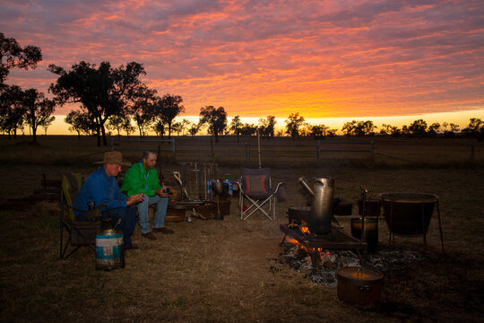 Two men sitting by a campfire at sunrise.