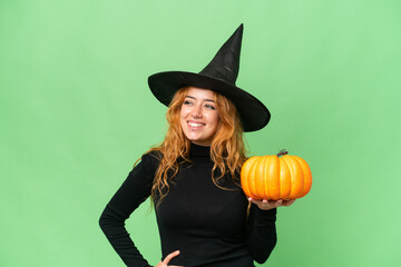 Young caucasian woman costume as witch holding a pumpkin isolated on green screen chroma key background posing with arms at hip and smiling