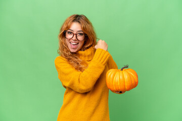 Young caucasian woman holding a pumpkin isolated on green screen chroma key background celebrating a victory