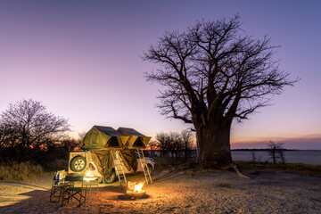 Africa - Camping in the wilderness with fire and sundowner in front of a Baobab Tree, Nxai Pan, Botswana - obrazy, fototapety, plakaty