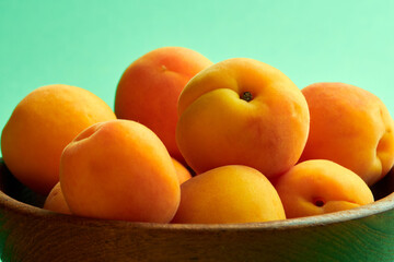 Bright ripe apricots in a wooden bowl on a green background