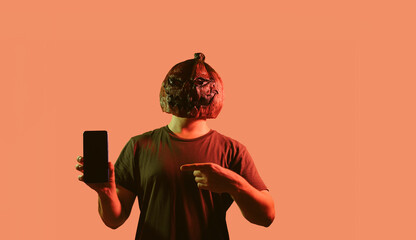 Man with pumpkin mask is pointing to a smartphone , advertising concept.