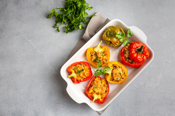 Stuffed peppers, halves of peppers stuffed with rice, dried tomatoes, herbs and cheese in a baking dish on a blue wooden table, top view. Vegetarian dish, stuffed vegetables