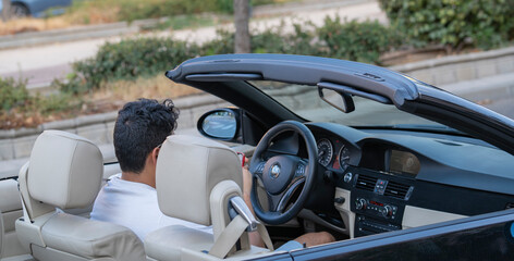 A man sitting inside in his convertible car waiting for someone while looking his mobile phone. business concepts