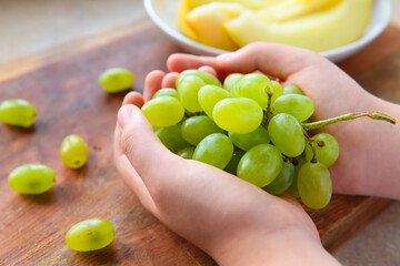 a woman's hand with green grapes, plate of melon slices on a wooden background, concept of fresh sweet fruits and healthy food