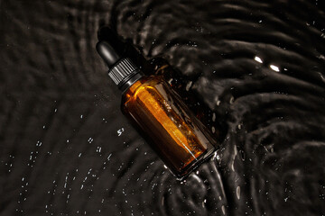 Cosmetic bottle with pipette in water. Amber glass. Waves, black background, dark waves, cosmetics, bottle, oil, toner, tonic, serum, acid.