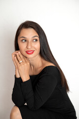 A sensual studio portrait of a beautiful young woman in a black dress with red lipstick on her lips. White background place for text