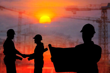 Silhouettes of male engineers watching construction drawings and men and women shaking hands to show cooperation with supervisors on construction site plans at sunset.