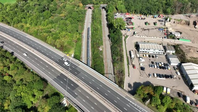 Commuter Train Speeding Under a Motorway in the UK Aerial View