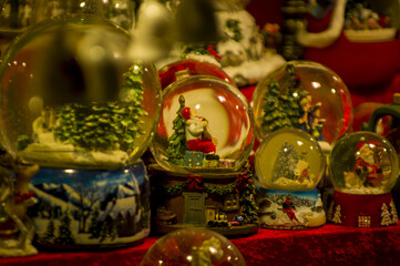 Fototapeta premium Advent Bazaar Stalls with glass, wooden, ceramic christmas souvenirs in shops. Close up of festive decorations for tree in winter street night market during new year's holiday. Illuminated fair kiosk