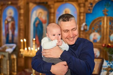happy godfather holding a little baptized child in his arms in church.