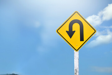 Traffic sign: Left U-turn sign on cement pole beside the rural road with white cloudy bluesky...