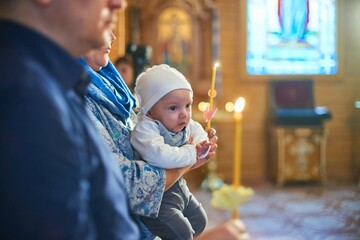 A small child at a baby christening ceremony in a church. the godfather holds a little boy in his...
