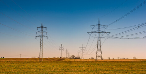 Beautiful farm landscape and high voltage power lines pylons in Germany at Autumn colors during sunset with blue sky. Concept of energy supply and energy crisis. - obrazy, fototapety, plakaty