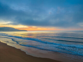 Obraz premium Peaceful sunrise over the ocean with small waves and clouds