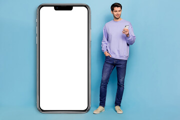 Full body photo of cute millennial brunet guy look telephone wear sweater jeans footwear isolated on blue background