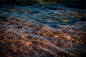 Macro Close-ups of clear ocean water with reflections, mossy rocks and beach sand  