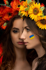 Two beautiful girls in flower wreaths of red poppy and yellow sunflower with ribbons. Concept Poland and Ukraine. Friendship and help Ukraine. Stop the war.