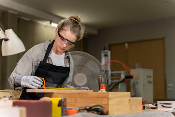 Portrait of a female carpenter measuring the dimensions of the wood prepared for her furniture creation in a furniture factory. with many tools and wood