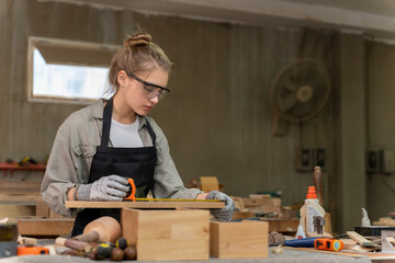 Portrait of a female carpenter measuring the dimensions of the wood prepared for her furniture creation in a furniture factory. with many tools and wood