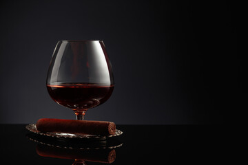 Snifter of brandy and cigar on a black background.