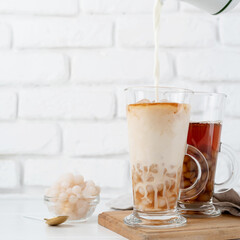 hand pouring milk into glass with iced bubble tea, white brick wall background