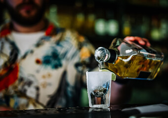 Bartender pouring strong alcohol drink into shot glass in bar
