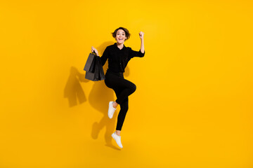 Fototapeta na wymiar Photo of positive lucky girl dressed formal shirt jumping high rising fist bags empty space isolated yellow color background