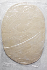 Rolled out Noodles dough covered with clingfilm, homemade noodles, process of making noodles, dough on pastry board	