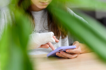 A teenage girl with a broken arm with a smartphone in her hands. Close-up of a girl with a bandage...