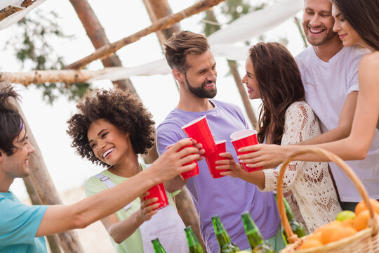 Photo of excited positive cheerful people hold plastic alcohol cups have good mood enjoy pastime outside