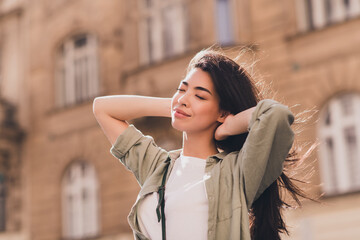 Photo of sweet lovely young asian woman wear khaki shirt enjoying fall sunshine arms head outside urban city street